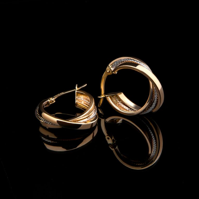 Close-up of luxurious gold earrings reflecting on a glossy black surface, showcasing elegant design.